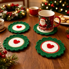 Load image into Gallery viewer, Green and White crochet coaster with a red heart design laid on a wooden table, with a Christmas wreath and some cookies, and a lighted Christmas in the background.
