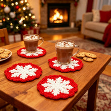 Load image into Gallery viewer, Red and white snowflake design crochet coasters with hot chocolate drink laid on a wooden table, with some cookies, shot in a living room setting with a lighted Christmas and fireplace in the background.
