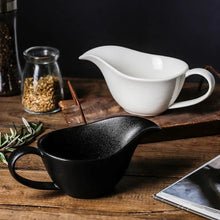 Load image into Gallery viewer, Curtis Ceramic Gravy Boat by Allthingscurated features an easy-to-hold handle and a narrow spout to ensure precise pouring without spills and drips. Available in white with a smooth, shiny glaze or black with a matte, rough finish. This versatile serveware with a capacity of 220ml or 7.4 fluid ounce is perfect for any occasion, formal or casual. 
