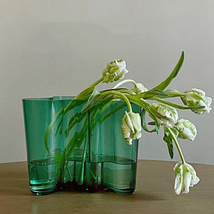 Green glass vase with green floral on a wooden surface. The Dayton Vase by Allthingscurated offers a beautiful asymmetrical design that feels both timeless and organic. Its sculptural, minimalist form brings a striking yet harmonious touch to any home interior. Available in clear, green and amber, it’s an unforgettable gift for housewarmings, weddings or holidays.