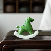 Load image into Gallery viewer, This Petite Ceramic Rocking Horse by Allthingscurated is a work of art. Crafted by hand from ceramic and decorated with a beautiful crackle pattern, it exudes a subtle far-eastern beauty and grace. Makes a perfect gift for those who appreciate quality craftsmanship and a treasured gift to any horse collector. Comes in green and azurerish white. Measures 9.8cm or 3.8 inches in height, 10.4cm or 4 inches in width and 4.2cm or 1.6 inches in depth. Featured here is a Green horse.
