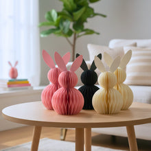 Load image into Gallery viewer, Five decorative bunny figures in pink, dark green, and beige on a wooden coffee table in a living room. This curated set of two Honeycomb Easter Bunnies by Allthingscurated instantly transforms any space into a festive Easter wonderland. Their adorable silhouettes add personality and warmth to your holiday décor. Quick assembly and compact storage, with proper care, they remain beautiful year after year. Comes in 5 delightful colors.
