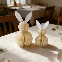 Load image into Gallery viewer, Two paper bunnies on a dining table with a blurred background. This curated set of two Honeycomb Easter Bunnies by Allthingscurated instantly transforms any space into a festive Easter wonderland. Their adorable silhouettes add personality and warmth to your holiday décor. Quick assembly and compact storage, with proper care, they remain beautiful year after year. Comes in 5 delightful colors.
