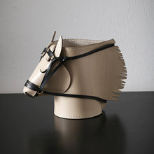 Load image into Gallery viewer, Product featured here is a beige leather horse-head shaped organizer with black leather straps and a fringe details, displayed on a dark reflective surface against a light gray background.
