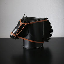 Load image into Gallery viewer, Product featured here is a black leather horse head-shaped organizer with brown leather straps and fringe details, displayed on a black surface against a light gray wall.
