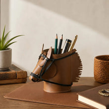 Load image into Gallery viewer, A brown faux leather desk organizer shaped like a horse head, filled with pens and pencils, styled on a wooden desk with a plant, books, and a basket in a warm indoor setting.
