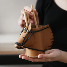 Load image into Gallery viewer, A person holds a brown leather pencil holder shaped like a horse head, with black straps and visible pencil shafts sticking out of the top, against a softly blurred indoor background.
