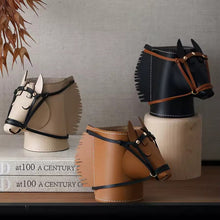 Load image into Gallery viewer, Three horse-head shaped cylindrical containers in beige, brown, and black, each styled with a leather bridle and mounted on wooden pedestals on a shelf.
