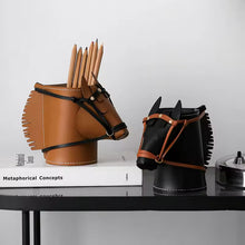 Load image into Gallery viewer, Two horse-shaped pencil holders on a black table against a white wall, one in brown leather and one in black leather, both with brown leather bridle details and holding wooden pencils.
