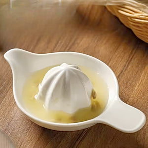White citrus juicer with lemon juice on a wooden surface. Ceramic Citrus Juicer by Allthingscurated features a classic reamer design with built-in pour spout that ensures precise pouring without spills. This single-piece tool is easy to store and indispensable in any bar or kitchen.