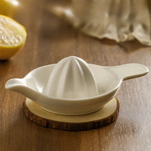 Load image into Gallery viewer, White ceramic citrus juicer on a wooden coaster with a lemon in the background. Ceramic Citrus Juicer by Allthingscurated features a classic reamer design with built-in pour spout that ensures precise pouring without spills. This single-piece tool is easy to store and indispensable in any bar or kitchen.
