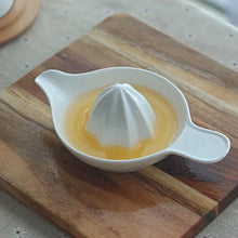Load image into Gallery viewer, White ceramic juicer with lemon juice on a wooden cutting board. Ceramic Citrus Juicer by Allthingscurated features a classic reamer design with built-in pour spout that ensures precise pouring without spills. This single-piece tool is easy to store and indispensable in any bar or kitchen.
