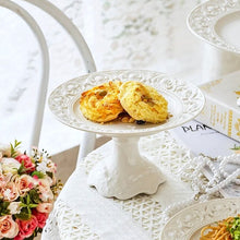 Load image into Gallery viewer, Juliette White Lace Dinnerware by Allthingscurated adds an elegant touch to your tabletop. This sophisticated set is crafted out of ceramic with a beautiful embossed lace rim, giving it a vintage touch.  The creamy white pieces come in a dinner plate and cake stand in 2 sizes for easy mixing and matching. They are perfectly sized for a main course, starters and desserts.
