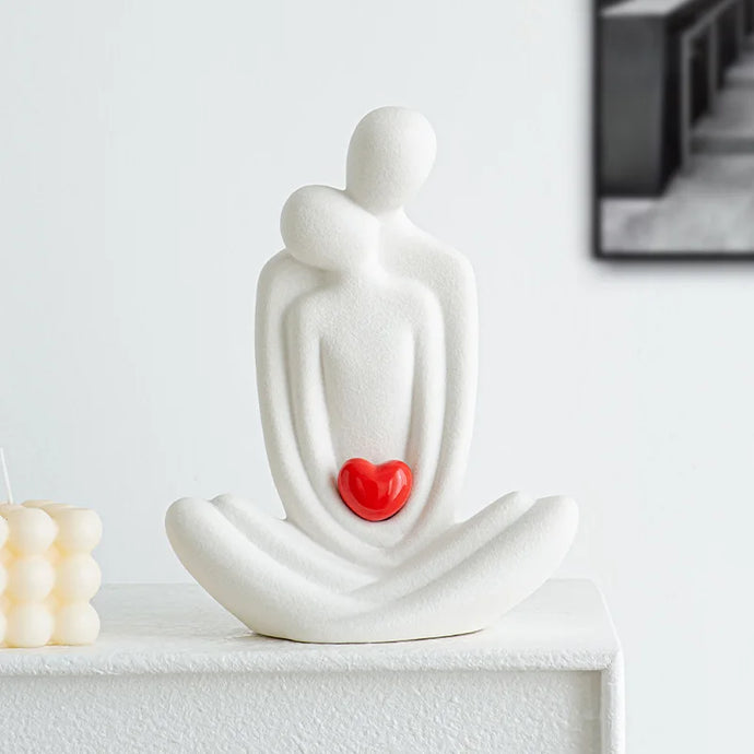 This romantic sculpture by Allthingscurated elegantly portrays a seated couple, locked in a tender embrace, their love and hearts held close. Sculpted in white ceramic, the piece highlights a striking red heart that symbolizes deep connection and passion. An ideal gift for Valentine’s Day or weddings, it offers a refined and timeless expression of affection.