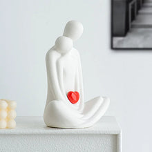 Load image into Gallery viewer, This romantic sculpture by Allthingscurated elegantly portrays a seated couple, locked in a tender embrace, their love and hearts held close. Sculpted in white ceramic, the piece highlights a striking red heart that symbolizes deep connection and passion. An ideal gift for Valentine’s Day or weddings, it offers a refined and timeless expression of affection.
