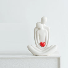 Load image into Gallery viewer, This romantic sculpture by Allthingscurated elegantly portrays a seated couple, locked in a tender embrace, their love and hearts held close. Sculpted in white ceramic, the piece highlights a striking red heart that symbolizes deep connection and passion. An ideal gift for Valentine’s Day or weddings, it offers a refined and timeless expression of affection.
