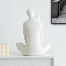 Load image into Gallery viewer, This romantic sculpture by Allthingscurated elegantly portrays a seated couple, locked in a tender embrace, their love and hearts held close. Sculpted in white ceramic, the piece highlights a striking red heart that symbolizes deep connection and passion. An ideal gift for Valentine’s Day or weddings, it offers a refined and timeless expression of affection.
