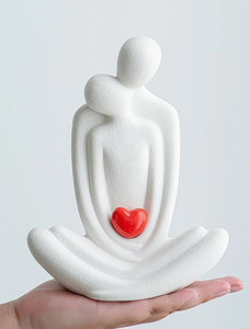This romantic sculpture by Allthingscurated elegantly portrays a seated couple, locked in a tender embrace, their love and hearts held close. Sculpted in white ceramic, the piece highlights a striking red heart that symbolizes deep connection and passion. An ideal gift for Valentine’s Day or weddings, it offers a refined and timeless expression of affection.