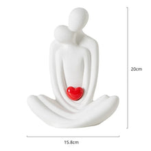 Load image into Gallery viewer, This romantic sculpture by Allthingscurated elegantly portrays a seated couple, locked in a tender embrace, their love and hearts held close. Sculpted in white ceramic, the piece highlights a striking red heart that symbolizes deep connection and passion. An ideal gift for Valentine’s Day or weddings, it offers a refined and timeless expression of affection.
