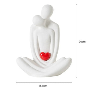 This romantic sculpture by Allthingscurated elegantly portrays a seated couple, locked in a tender embrace, their love and hearts held close. Sculpted in white ceramic, the piece highlights a striking red heart that symbolizes deep connection and passion. An ideal gift for Valentine’s Day or weddings, it offers a refined and timeless expression of affection.