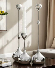 Load image into Gallery viewer, Three silver candle holders on a table with a neutral background. Lumea Silver Candle Holders by Allthingscurated feature a striking trio of sculptural pieces that blend contemporary design with timeless elegance. Each holder features a distinctive water droplet base that anchors a sleek, minimalist silhouette, creating an art deco-inspired statement on its own. this set makes an exceptional wedding gift for couples seeking sophisticated home décor that transcends occasion.
