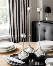 Load image into Gallery viewer, Decorative silver candle holders on a table with a blurred background. Lumea Silver Candle Holders by Allthingscurated feature a striking trio of sculptural pieces that blend contemporary design with timeless elegance. Each holder features a distinctive water droplet base that anchors a sleek, minimalist silhouette, creating an art deco-inspired statement on its own. this set makes an exceptional wedding gift for couples seeking sophisticated home décor that transcends occasion.
