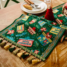 Load image into Gallery viewer, Decorative Christmas table runner with tassels on a wooden table. Elevate your holiday entertaining with this Merry Christmas Jacquard Table Runner by Allthingscurated. Inspired by the joy of gift-giving, this table runner features an array of gift box motifs rendered in rich jewel tones, this piece showcases beautiful embroidery complemented by pretty tassels. Perfect for elevating your holiday tablescape, making every feast and gathering truly memorable. 
