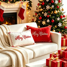 Load image into Gallery viewer, Two rectangular “Merry Christmas” throw pillows on a white sofa in a room with festive home decor, featuring a Christmas tree and stockings by a fireplace in the background.
