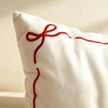 Load image into Gallery viewer, White throw pillow featuring red embroidered stitching of a ribbon bow in the corner, perfect for seasonal home decor.
