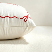 Load image into Gallery viewer, White throw pillow with close zipper featuring red embroidered stitching of a ribbon bow in the corner, perfect for seasonal home decor.
