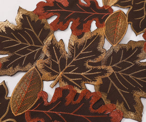 Close-up of embroidered leaves with brown, red, and gold colors on a white background. By Allthingscurated.