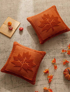 Two orange pillows with maple leaf patterns on a textured surface with decorative items. The Velour Maple Leaf Cushion Cover by Allthingscurated is a beautiful way to bring the warmth of fall into your home. With its elegant tufted pumpkin design and soft velour fabric, it offers both comfort and style. Perfect for autumn and Thanksgiving, this decorative pillow adds a cozy, inviting touch to any space.