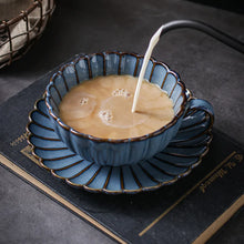 Load image into Gallery viewer, Tea served in a blue ceramic cup and saucer with a decorative interior being filled with milk on a dark surface. Japanese Chrysanthemum Cup and Saucer by Allthingscurated is inspired by the flower’s perfect symmetry and stunning beauty in the Japanese culture. Crafted from porcelain, it’s a beautiful set to entertain friends and family for afternoon teas at home.
