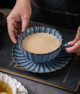 Blue ceramic cup set with a decorative interior filled with tea, held by a person. Japanese Chrysanthemum Cup and Saucer by Allthingscurated is inspired by the flower’s perfect symmetry and stunning beauty in the Japanese culture. Crafted from porcelain, it’s a beautiful set to entertain friends and family for afternoon teas at home.