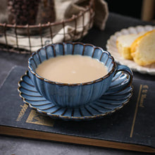 Load image into Gallery viewer, Blue ceramic cup with saucer containing a tea placed on a dark surface. Japanese Chrysanthemum Cup and Saucer by Allthingscurated is inspired by the flower’s perfect symmetry and stunning beauty in the Japanese culture. Crafted from porcelain, it’s a beautiful set to entertain friends and family for afternoon teas at home.
