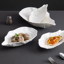 Load image into Gallery viewer, White oyster-shaped bowls with food on a dark surface. Oyster Shape Serving Dish by Allthingscurated is elegantly crafted in pristine white ceramic to mirror the contours and texture of the elegant oyster. The striking serve ware comes in multiple sizes for plating appetizers or main courses.
