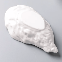Load image into Gallery viewer, Underside of the white oyster dish on a gray background. Oyster Shape Serving Dish by Allthingscurated is elegantly crafted in pristine white ceramic to mirror the contours and texture of the elegant oyster. The striking serve ware comes in multiple sizes for plating appetizers or main courses.
