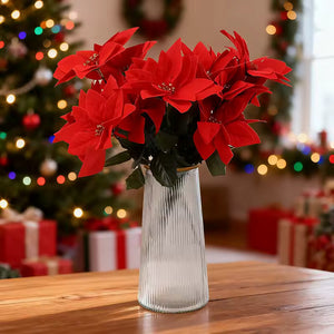 Bouquet of red poinsettias in a clear vase on a wooden table with a festive background. Bring the true spirit of the holidays into your home with this bundle of 5 classic red Faux Poinsettia by Allthingscurated. These timeless blooms complement any festive palette and instantly evokes Christmas cheer.