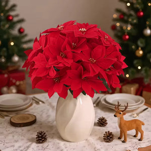Bouquet of red poinsettias in a white vase on a decorated table with Christmas trees in the background. Bring the true spirit of the holidays into your home with this bundle of 5 classic red Faux Poinsettia by Allthingscurated. These timeless blooms complement any festive palette and instantly evokes Christmas cheer.