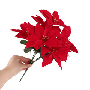 Red poinsettia flowers held by a hand on a white background. Bring the true spirit of the holidays into your home with this bundle of 5 classic red Faux Poinsettia by Allthingscurated. These timeless blooms complement any festive palette and instantly evokes Christmas cheer.