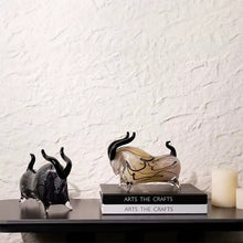 Load image into Gallery viewer, Decorative bull sculptures on books with a candle against a textured white wall. Rex Decorative Bull by Allthingscurated are meticulously handmade from high quality glass. Comes in three striking finishes—an all-all black edition or two-tone variants featuring bold graphic elements. Rex brings contemporary flair and bold energy to any room. More than décor, it’s an ideal gift for those born under the Ox zodiac and Taurus sign.
