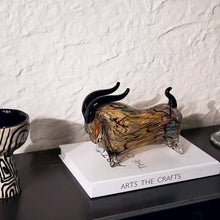 Load image into Gallery viewer, Glass bull sculpture on a book with a white textured wall background. Decorative bull sculptures on books with a candle against a textured white wall. Rex Decorative Bull by Allthingscurated are meticulously handmade from high quality glass. Comes in three striking finishes—an all-all black edition or two-tone variants featuring bold graphic elements. Rex brings contemporary flair and bold energy to any room. More than décor, it’s an ideal gift for those born under the Ox zodiac and Taurus sign.
