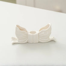 Load image into Gallery viewer, Fashion Bow Candle Holder by Allthingscurated spots a distinctive knot design, beautiful yet practical. Perfect for wedding celebrations, home styling, or to infuse warmth and romance into any living space. Available in three colors and 2 sizes. Shown here is a small size White bow candle holder on a white background.
