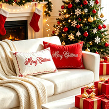 Load image into Gallery viewer, Cream and red embroidered Merry Christmas throw pillows rest on a white sofa in a room styled with festive home decor, featuring a fireplace with stockings, wrapped gifts, and a decorated Christmas tree.
