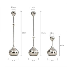 Load image into Gallery viewer, Lumea Silver Candle Holders by Allthingscurated feature a striking trio of sculptural pieces that blend contemporary design with timeless elegance. Each holder features a distinctive water droplet base that anchors a sleek, minimalist silhouette, creating an art deco-inspired statement on its own. this set makes an exceptional wedding gift for couples seeking sophisticated home décor that transcends occasion. Featured here is a set of 3 candle holders.
