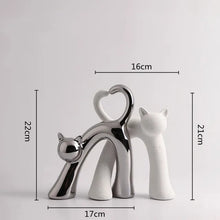 Load image into Gallery viewer, These Cat Couple Love Figurines by Allthingscurated are perfect for cat lovers. Made of ceramic, they feature a pair of cute and whimsical cats in contrasting colors, with their tails entwined to form a heart shape. A romantic and unique gift for any occasion.  This set features a pair of silver and white cats.

