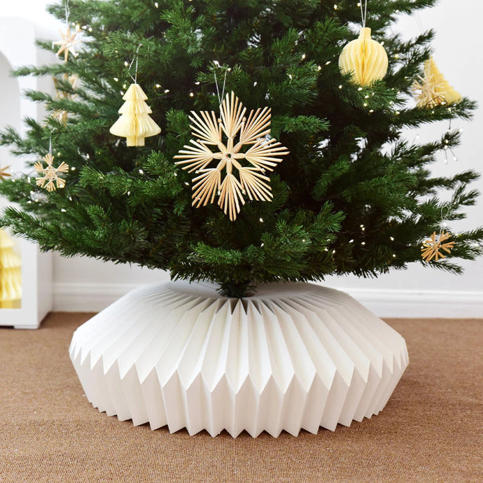 Decorative Christmas tree with a white paper base and gold ornaments.  Transform your holiday setup with the striking Honeycomb Christmas Tree Collar by Allthingscurated. Crafted from premium paper with easy setup, its distinctive pleated design delivers sophisticated visual interest while concealing the tree base with understated elegance. The crips white finish works beautifully with any tree style.