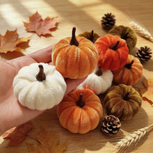 Load image into Gallery viewer, A hand holds a small plush white velvet pumpkin next to several small decorative velvet pumpkins in orange, brown, arranged on a wooden surface with autumn leaves, pinecones, and wheat stalks.
