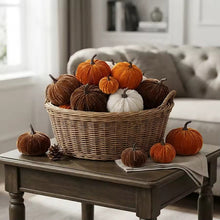 Load image into Gallery viewer, A large woven wicker basket filled with assorted decorative pumpkins in orange, brown, and white styled on a dark wooden table in a cozy living room setting.
