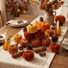 Load image into Gallery viewer, A styled autumn tabletop arrangement with multiple small velvet pumpkins in orange, rust, and cream tones, plus pinecones, cinnamon sticks, amber candle holders, plates, and a ceramic pitcher with fall foliage on a wooden table.
